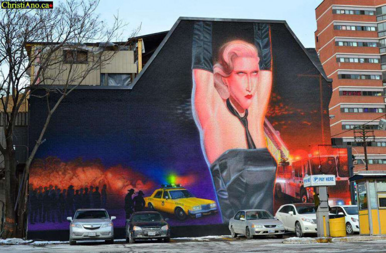 Mural on the side of a building with a person's arms upstretched wearing a tie, black dress and gloves