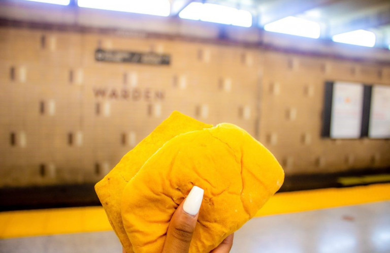 Hand with a manicured nail holding a patty in coco bread at Warden Station