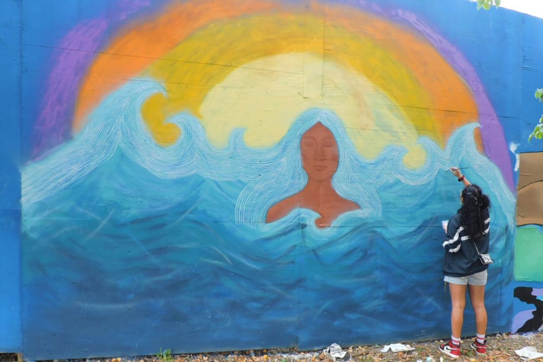 Mural of a woman surrounded by waves and the artist painting details